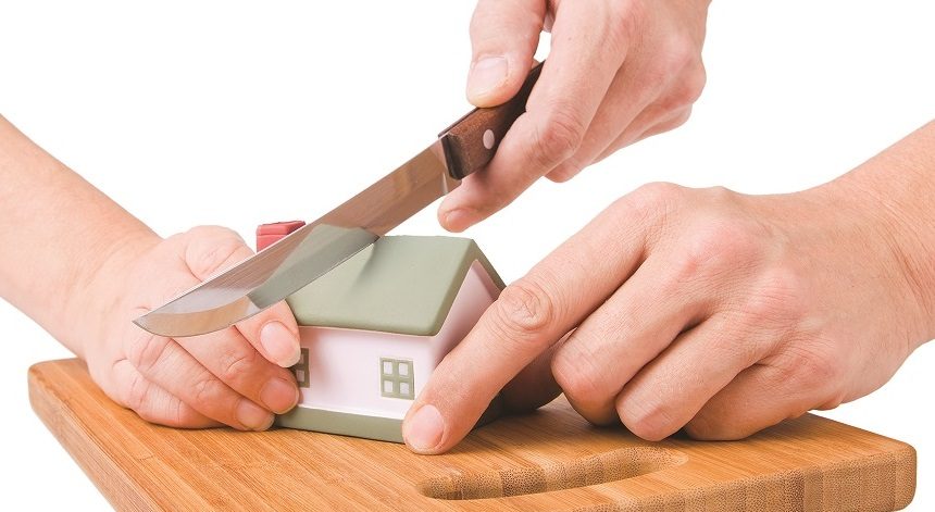 Sale of Former Matrimonial Home in a divorce settlement, represented by hands cutting a model house with a knife on a wooden chopping board.