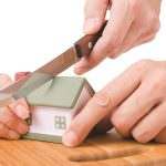 Sale of Former Matrimonial Home in a divorce settlement, represented by hands cutting a model house with a knife on a wooden chopping board.