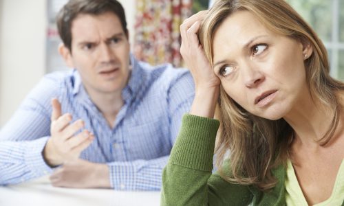 A concerned woman appears stressed while a man gestures in mid-conversation, possibly indicating a disagreement between them. This situation might require Mediation Readiness to resolve the misunderstanding effectively.