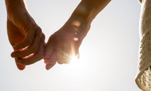 Two people in a civil union holding hands backlit by the sun, conveying a sense of companionship.