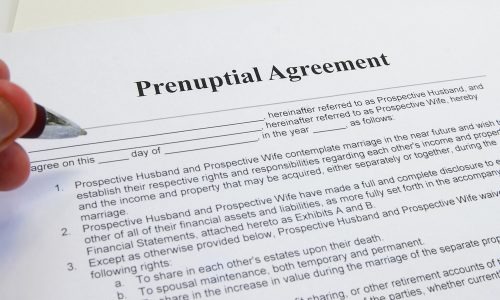 A hand holding a pen over a prenuptial agreement document, ready to sign.