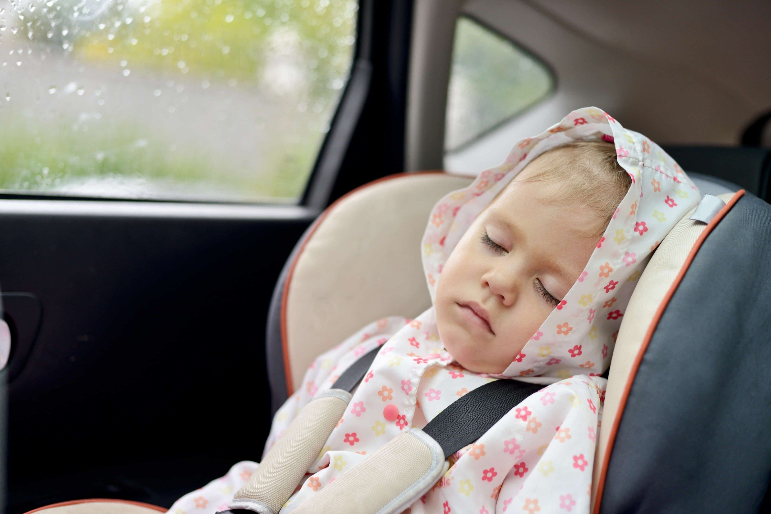 Toddler sleeping in a car seat with a raindrop-covered window in the background, amidst a relocation.