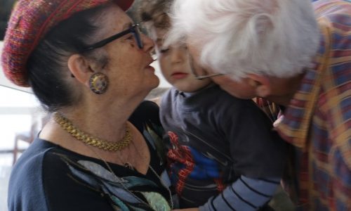 Two grandparents affectionately kiss their grandchild on the cheeks.